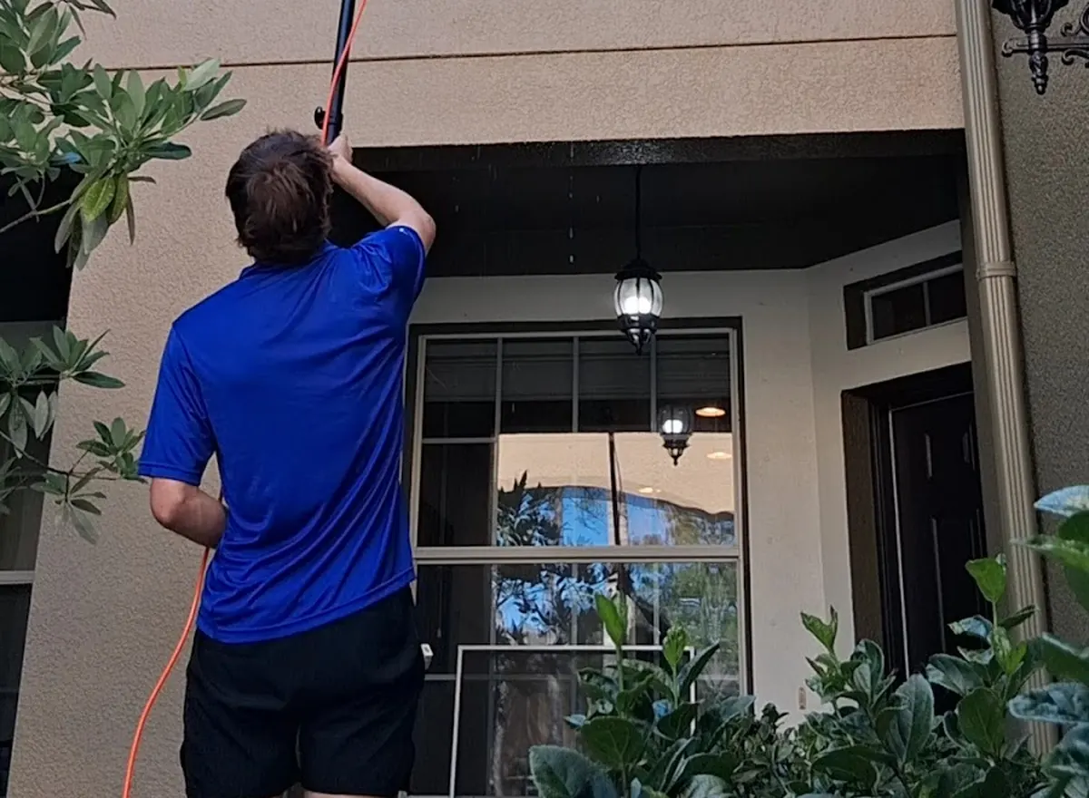 Window washer cleaning second-story windows of a home with an extension pole
