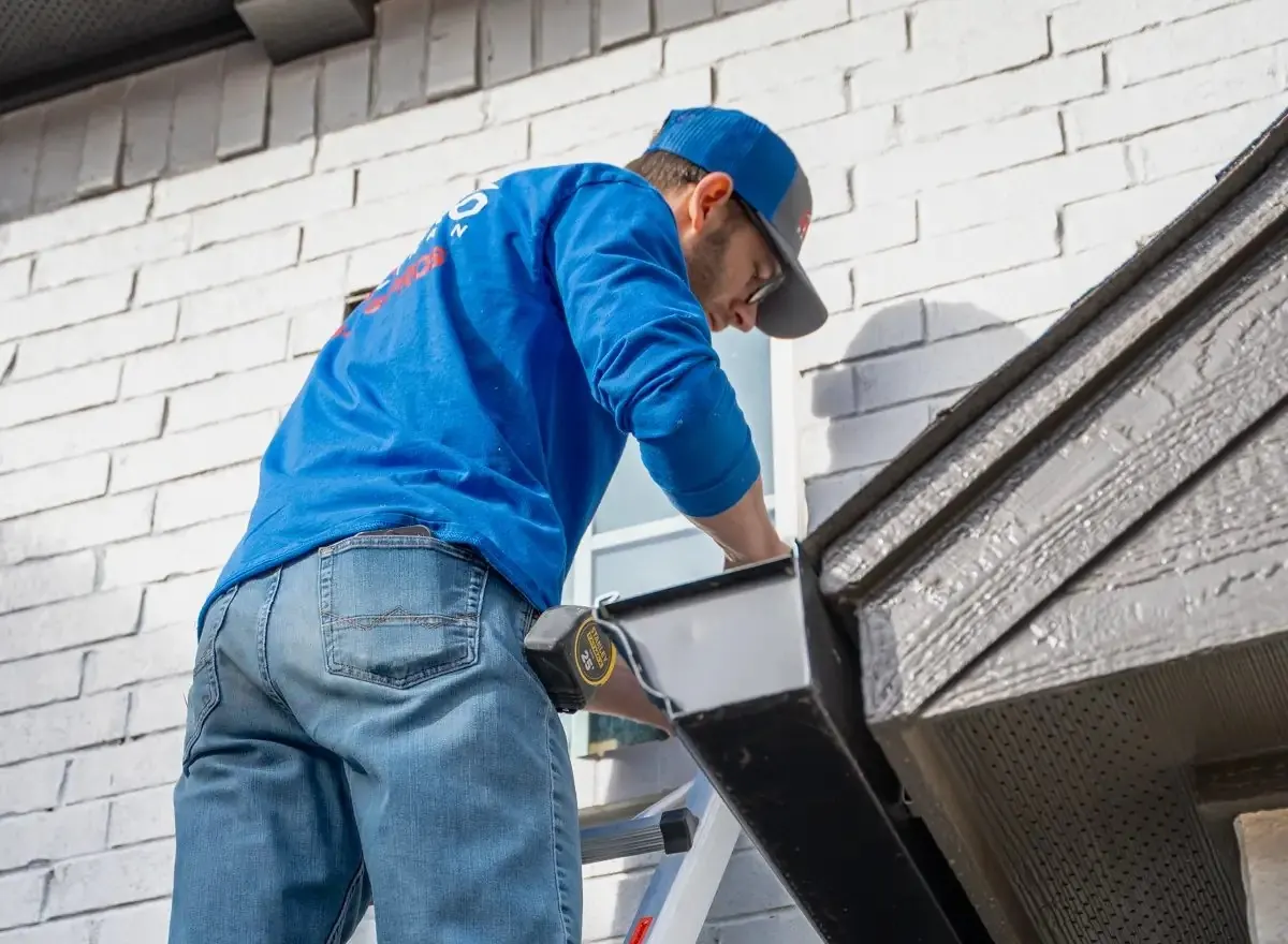 Gutter cleaner on a ladder clearing a roof gutter on a house