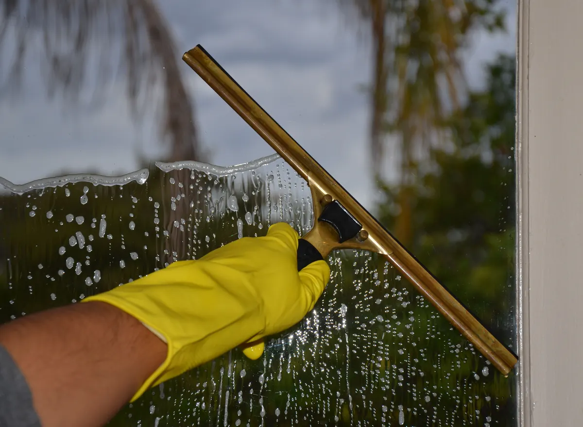 Brass squeegee removing water spots from window glass