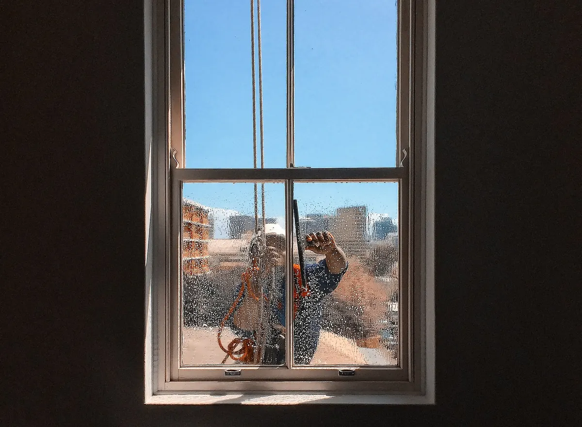 Window cleaner working outside a sash window, seen from inside the room